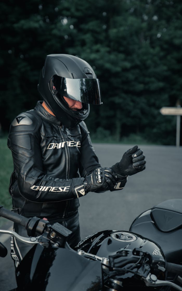 Motorcyclist in black leather gear adjusting gloves on a road in France