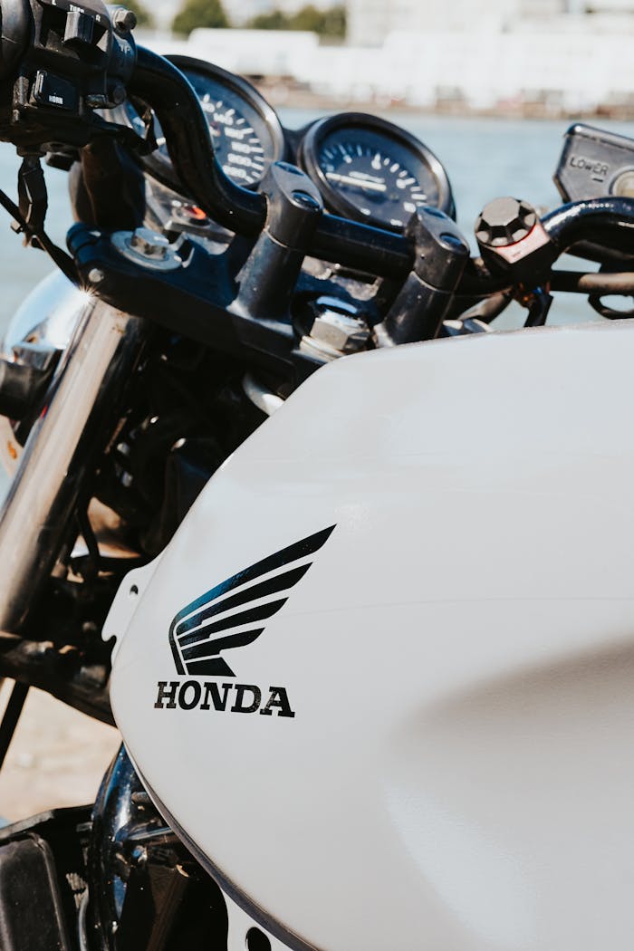 Detailed close-up shot of a Honda motorcycle fuel tank featuring the Honda logo in an outdoor setting.